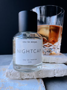 Who is Elijah Nightcap perfume bottle sitting on thin sandstone block with whisky nightcap cocktail placed in the background against a black backdrop