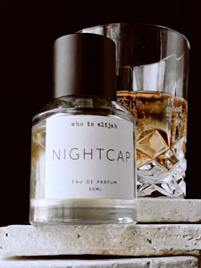 Who is Elijah Nightcap perfume bottle sitting on thin sandstone block with whisky nightcap cocktail placed in the background against a black backdrop